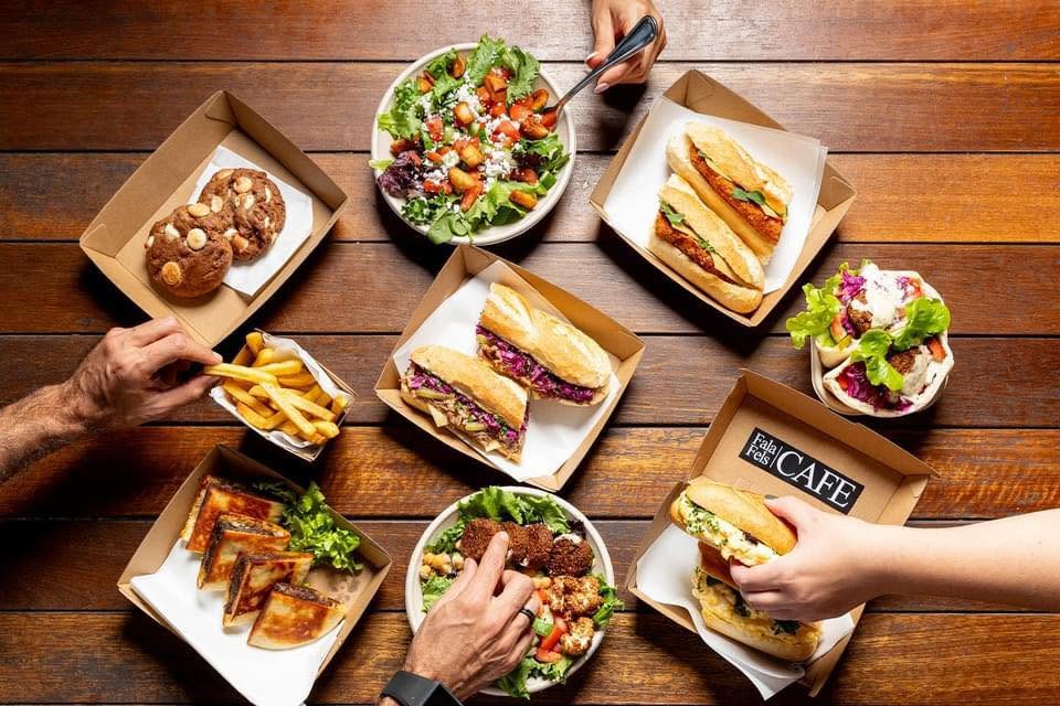 Overhead spread of Fala Fels cookies, salad, baguettes, chips, burek and a falafel pocket in a branded box